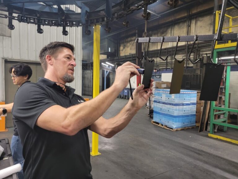 Technician checking paint thickness on test plate